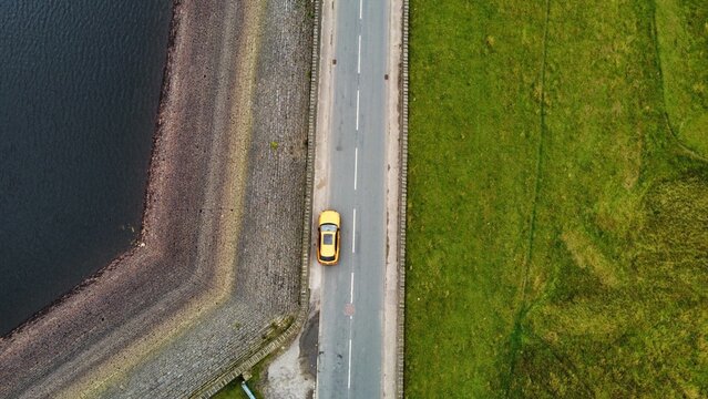 Aerial view of a modern car parked up on a road surrounded by countryside. 