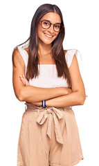 Wall Mural - Young hispanic woman wearing casual clothes and glasses happy face smiling with crossed arms looking at the camera. positive person.