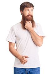 Sticker - Handsome young red head man with long beard wearing casual white tshirt with hand on chin thinking about question, pensive expression. smiling with thoughtful face. doubt concept.