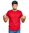 Young handsome man wearing casual red tshirt pointing down looking sad and upset, indicating direction with fingers, unhappy and depressed.