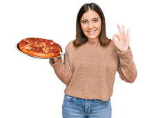 Young Beautiful Woman Holding Italian Pizza Doing Ok Sign With Fingers, Smiling Friendly Gesturing Excellent Symbol