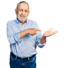 Sticker - Senior man with grey hair and beard wearing casual blue shirt amazed and smiling to the camera while presenting with hand and pointing with finger.