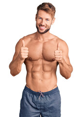 Young caucasian man standing shirtless success sign doing positive gesture with hand, thumbs up smiling and happy. cheerful expression and winner gesture.