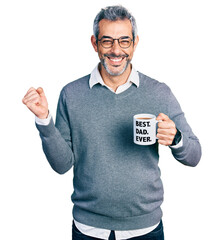 Wall Mural - Middle age hispanic man with grey hair drinking mug of coffee with best dad ever message screaming proud, celebrating victory and success very excited with raised arm