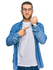 Poster - Young caucasian man wearing casual clothes in hurry pointing to watch time, impatience, looking at the camera with relaxed expression