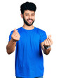 © Krakenimages.com - Young arab man with beard wearing casual blue t shirt doing money gesture with hands, asking for salary payment, millionaire business
