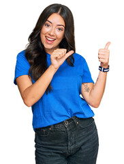 Beautiful brunette young woman wearing casual clothes pointing to the back behind with hand and thumbs up, smiling confident
