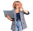 Young blonde woman with curly hair working using laptop smiling happy and positive, thumb up doing excellent and approval sign