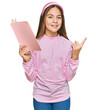 © Krakenimages.com - Beautiful brunette little girl reading a book smiling happy pointing with hand and finger to the side