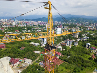 Wall Mural - Close-up of a yellow construction crane on the background of mountains, private sector on a sunny day, view from a drone