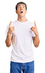 Wall Mural - Young handsome man wearing casual white tshirt amazed and surprised looking up and pointing with fingers and raised arms.