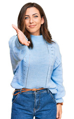 Wall Mural - Young brunette woman wearing casual winter sweater smiling cheerful offering palm hand giving assistance and acceptance.