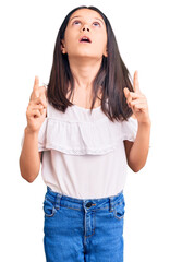 Canvas Print - Beautiful child girl wearing casual clothes amazed and surprised looking up and pointing with fingers and raised arms.