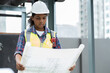 © amorn - Woman engineer working with construction building blueprint at sewer pipes area at construction site on rooftop of building