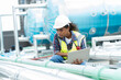 © amorn - Female engineer work using laptop computer for checks or maintenance in sewer pipes area at construction site. African American woman engineer working in sewer pipes area at rooftop of building