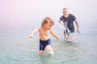© Anna - Father and toddler son playing in the sea in cloudy foggy weather. Dad catching up his child in water, summer vacation concept