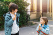 © Anna - Two brothers eating soft ice cream in waffle cones outdoors. Siblings spending time together. Toddler boy showing tongue to his brother.