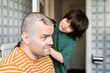 © Anna - Teenager boy cutting father's hair with electronic shaver in bathroom at home. Happy fatherhood, quarantine haircut.