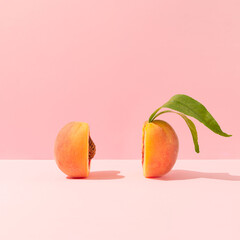 fresh ripe organic peach with pit and leaves cut in half against bright peach pink background. minim