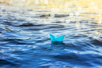 paper origami ship sails on blue water, travel and adventure, dreams and hopes concept