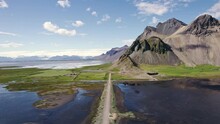Aerial view flying over Vestrahorn mountain and black sand beach by the sea on sunny day in summer at Stokksnes Peninsula, Iceland