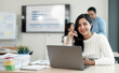 © NAMPIX - Attractive asian young confident businesswoman sitting at the office table with group of colleagues in the background, working on laptop computer