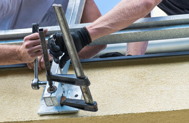 Construction workmans at assembling steel structure to building wall. Closeup of workers hands with ratchet wrench when screwing and tightening metal guard rail clamped in fastening device on terrace.