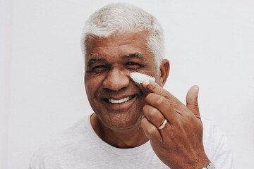 Happy senior man applying a moisturizing cream on his face