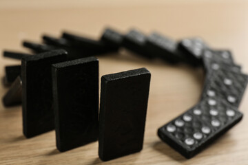 Wall Mural - Black domino tiles falling on wooden table, closeup