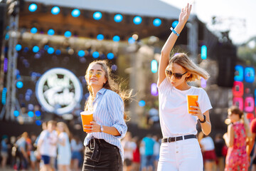 Wall Mural - Two young woman  having a great time at a music festival. Happy girlfriends rinking beer and having fun at Beach party. Summer holiday, vacation concept.