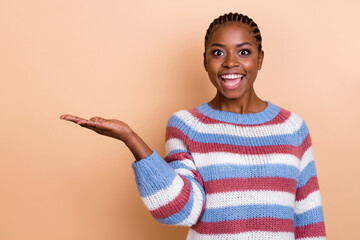 Photo of impressed braids hairstyle young lady hold empty space wear striped sweater isolated on beige color background