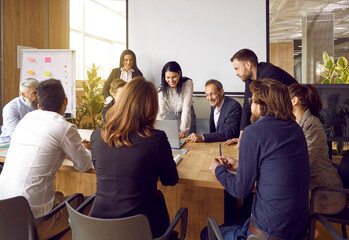 Wall Mural - Corporate business. Happy business team gathered at table in office and laughs working together at corporate briefing. Friendly colleagues discuss work issues and enjoy teamwork during staff meeting.