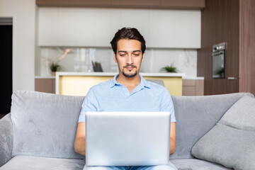 Handsome man sitting on the couch and working on laptop at home. Online education and distant work concept