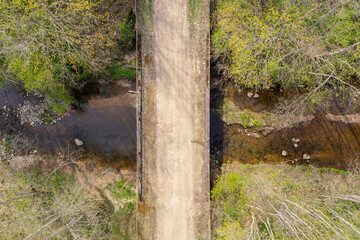 Wall Mural - Aerial top down view of rural gravel road and bridge over river flowing through forest in spring