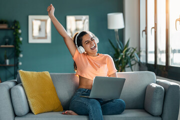 Wall Mural - Pretty woman celebrating something while working with laptop sitting on a couch at home.