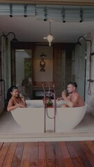 Wall Mural - Asian women and European men relax in a bathtub during vacation, a luxury holiday. Couple men and woman drinking wine in the bathtub during a vacation in a luxury resort