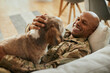© Drazen - Happy African American military man enjoys with his dog at home.