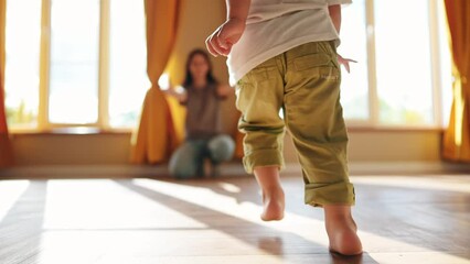 baby runs to mom at home. a child with bare legs runs across the floor to his mother against a sunny