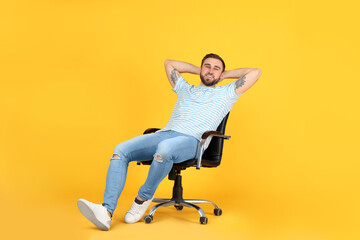 Wall Mural - Young man relaxing in comfortable office chair on yellow background