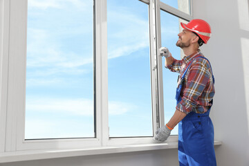 Poster - Worker in uniform installing plastic window indoors