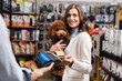 Smiling customer paying with credit card and holding poodle in pet shop