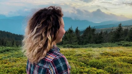 Wall Mural - beautiful curly girl looking at the  mountains against the backdrop of the Carpathian and forests at sunset blue sky tourism travel outdoor recreation vacation walks weekend back view without face