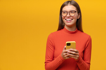 Smiling woman having fun browsing social media network on phone on yellow copy space background