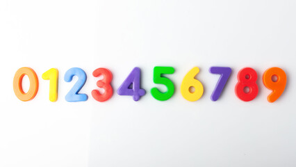Multi-colored plastic magnetic numbers on a white background from 0 to 9 top view sequentially.