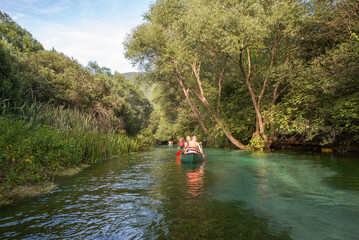 View of a group of people having a canoe experience on a natural blue river. Green landscape background