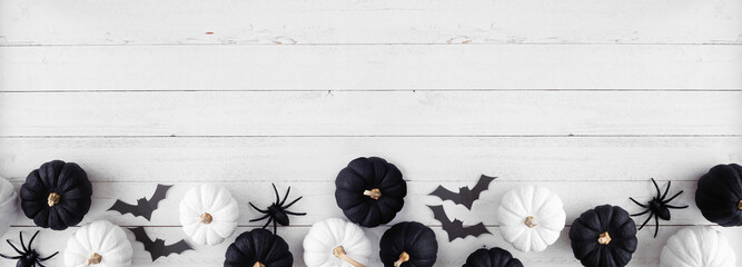Wall Mural - Halloween bottom border of black and white pumpkins with bats and spiders. Top down view over a white wood banner background. Copy space.