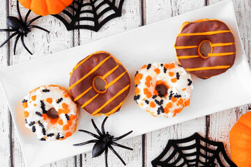Wall Mural - Spooky Halloween themed donuts. Above view table scene on a white wood background.