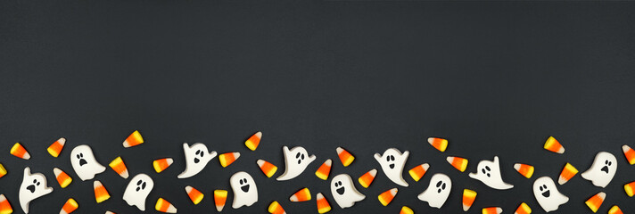  Halloween bottom border of candy corn and spooky chocolate ghosts. Top down view on a black banner background. Copy space.