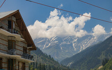 14 June, 2022, Manali, Himachal Pradesh. View Of Himalayan Valley Of Himachal Pradesh. Majestic Mountains Covered With Pine Forests. Snow Peaks, Drifting Clouds In Blue Sky. Hotel Building In Front.