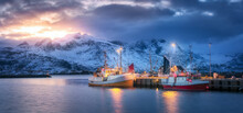 Fishing Boats On The Sea, Snowy Mountains, Colorful Sky With Clouds At Sunrise In Lofoten Islands, Norway. Winter Landscape With Boats, Harbor, Lights, Houses With Illumination, Rocks In Snow At Dawn